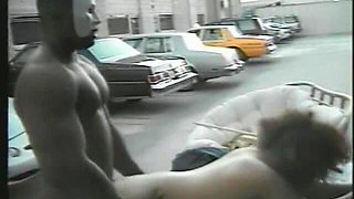 Muscular Stranger in White Superhero Mask Drills Ebony Chick on the Parking of Shopping Mall